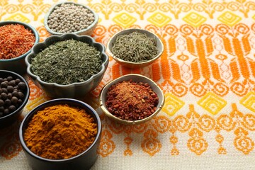 Many different aromatic spices in bowls on table with cloth, closeup. Space for text