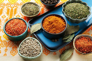 Many different aromatic spices in bowls on table with cloth, closeup