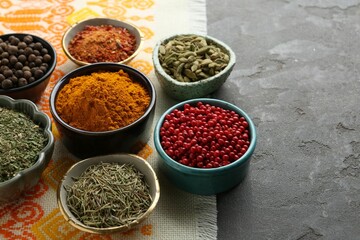 Many different aromatic spices in bowls on grey table with cloth, closeup. Space for text