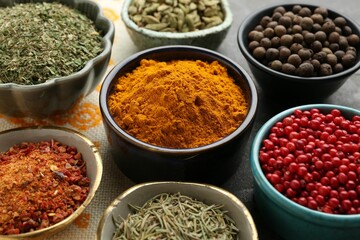 Many different aromatic spices in bowls on grey table with cloth, closeup