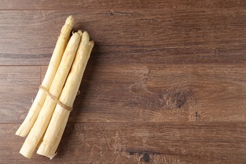 Bunch of raw white asparagus spears on wooden table, top view. Space for text