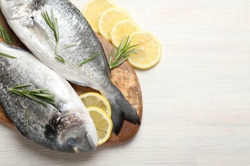 Organic seafood. Fresh raw dourade fish, lemon slices and rosemary on white wooden table, flat lay....