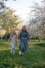 Fototapeta premium A mother and daughter are running through a blooming apple orchard. They are talking to each other. The concepts of family, mother, and child, and modern child-rearing.