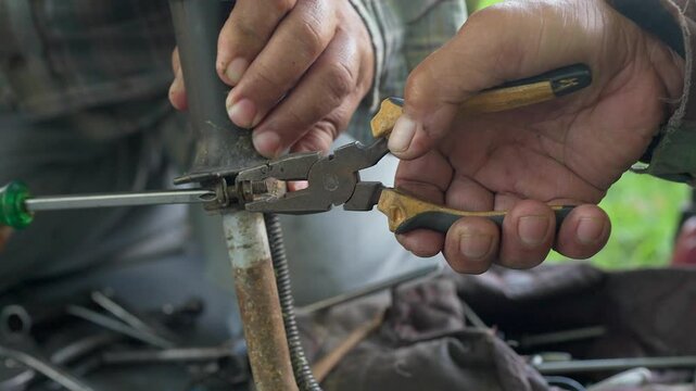 Closeup shot of the hands of two persons using pliers and screwdriver to work on a rusted metal rod