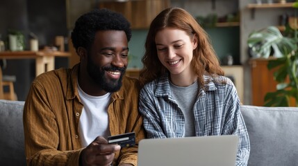 Smiling young couple making shopping online with credit card and laptop at home. Happy multiethnic couple holding debit card while buying on ecommerce site using laptop. , no logos, no brands
