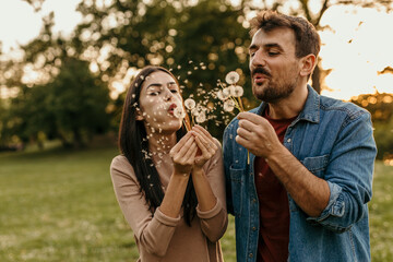 Happy couple blowing dandelion seeds in a meadow at sunset