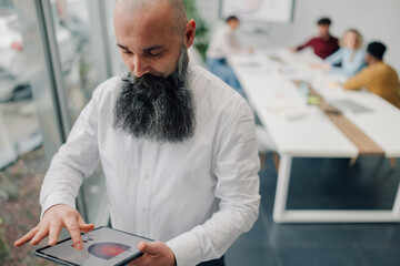 Businessman using digital tablet showing charts in modern office with coworkers in background