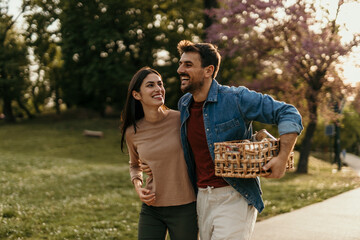 Happy couple carrying picnic basket walking in park