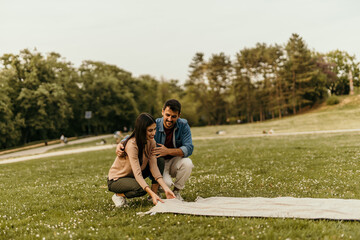 Happy couple preparing picnic blanket in city park