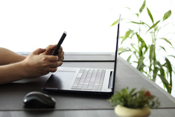 Close-Up of Person Typing on Smartphone at Desk in Front of Laptop Computer