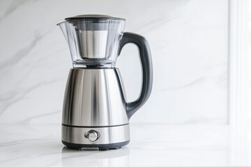 A modern, brushed-metal tea maker with a glass top sits elegantly on a clean white marble surface, showcasing simplicity.