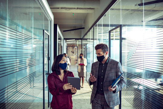 Coworkers wearing face masks walking and talking in modern office hallway - Powered by Adobe
