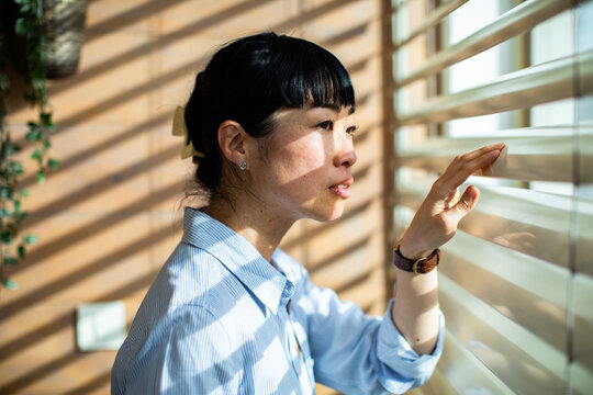 Woman looking out window through blinds with sunlight shadows