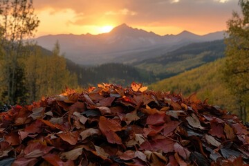A pile of colorful autumn leaves sits before a mountain landscape at golden hour.