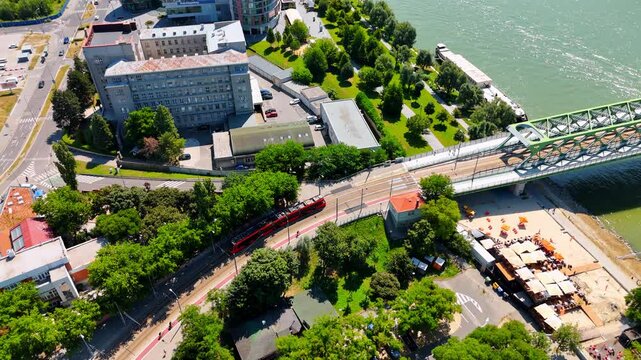Red tram leaves the Old Bridge and moves to the old part of the city. Drone footage above sunny Bratislava, Slovakia.
