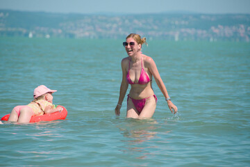 girl swims on inflatable toy accompanied by mother
