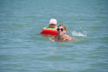 girl swims on inflatable toy accompanied by mother