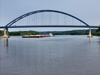 Fototapeta premium View of a large barge comming down the Mississippi River soon to pass under a tied-arch bridge.
