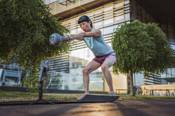 Japanese mature woman filming a workout video with kettle bell weight