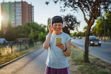 Smiling japanese woman use cellphone while jogging on the street