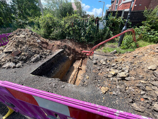 A construction site with exposed ground showing soil layers, red underground cables, and...