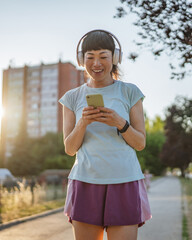 Smiling japanese woman use cellphone while jogging on the street
