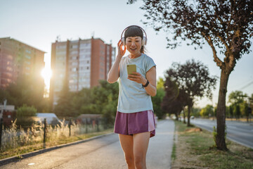 Smiling japanese woman use cellphone while jogging on the street