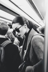 Stylish woman in sunglasses riding a crowded subway. Black and white street photography captures urban fashion, mystery, and solitude in public transport. Elegant, moody, cinematic atmosphere.