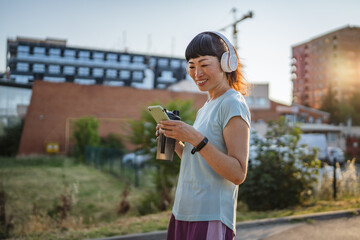 japanese woman drink protein shake and use mobile phone after jogging