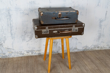 Two vintage suitcases stand on a stool against a white wall. The concept of retro travel and retro design.