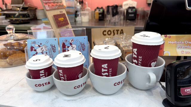 Warsaw, Poland - June 28, 2025: Costa Coffee cups arranged in various sizes on counter with pastries nearby