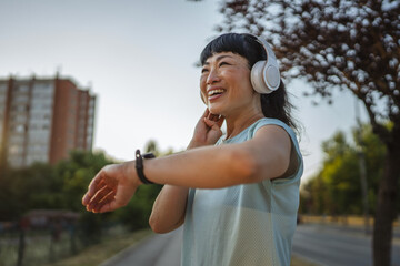 Happy japanese woman runner with headphones checking smart watch