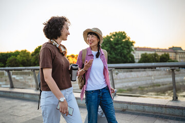two women friends with suitcases discuss and walk on bridge