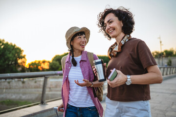 two women friends with suitcases discuss and walk on bridge
