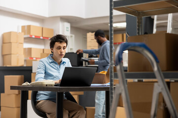 Female business owner works on a laptop in a local storehouse, focusing on shipping logistics for...