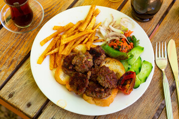 Spicy kofte served with fresh cucumber, bread, vegetables and French fries on a rustic wooden board