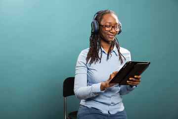 Attractive young black woman with wireless headphones touches her tablet while watching videos....