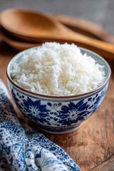 A bowl of white rice with a blue and white floral pattern sits on a wooden surface next to a matching cloth