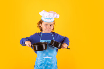 Kid chef cook with cooking pot stockpot. Cooking children. Chef kid boy in form of cook. Child boy with apron and chef hat preparing a healthy meal on studio isolated background. Cooking process.