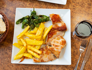 Service plate containing baked piece of pork with potato slices and green peppers