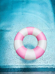 Swimming ring with pink and white stripes in a blue outdoor pool. Poolside atmosphere. Pink float.