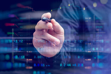 A close-up of a hand with a stylus interacting with a digital stock market chart. The overlay of candlestick graphs, buy and sell signals and numerical data.