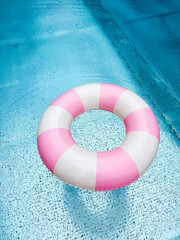Swimming ring with pink and white stripes in a blue outdoor pool. Poolside atmosphere. Pink float.