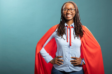 African american woman in red cape and blue shirt, hands on waist, smiling brightly at camera....
