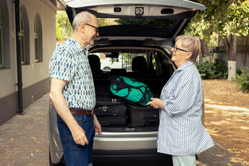 Senior people prepare their automobile for an exciting road trip during summer, loading suitcases...
