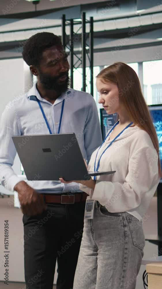 Poster vertical video junior dev and colleague in office reviewing ai system metrics, monitoring performanc