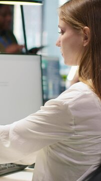 Vertical video Female technician coding with AI language model assistance in startup office, listening music. Young woman wearing headphones integrating LLM assistant suggestions into code editor