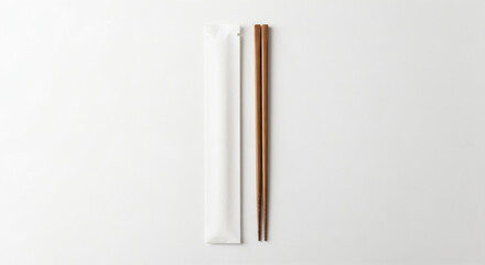 Pair of wooden chopsticks placed next to a simple white paper sleeve. The chopsticks are laid out parallel on a light-colored background.