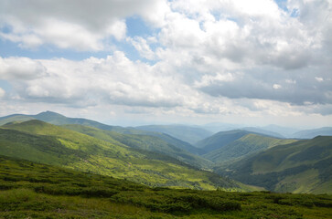 Beautiful green mountains ans hills with a mix of grasslands and shrubs spread across the horizon beneath a partly cloudy sky, embodying serenity and natural beauty. Svydovets, Carpathians, Ukraine