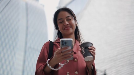 Smiling businesswoman using smartphone and drinking coffee in city center